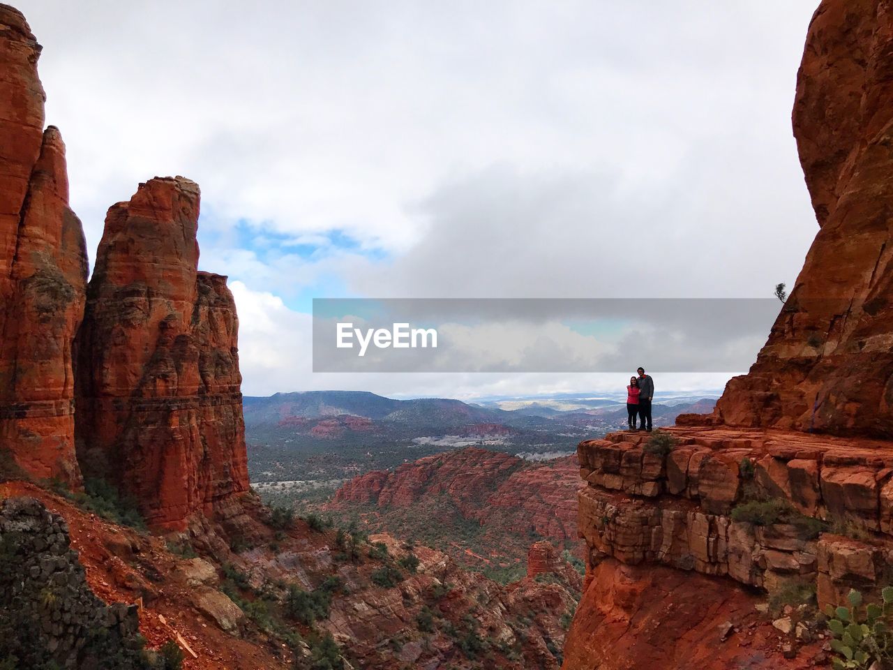 Couple standing on rocky mountains against cloudy sky