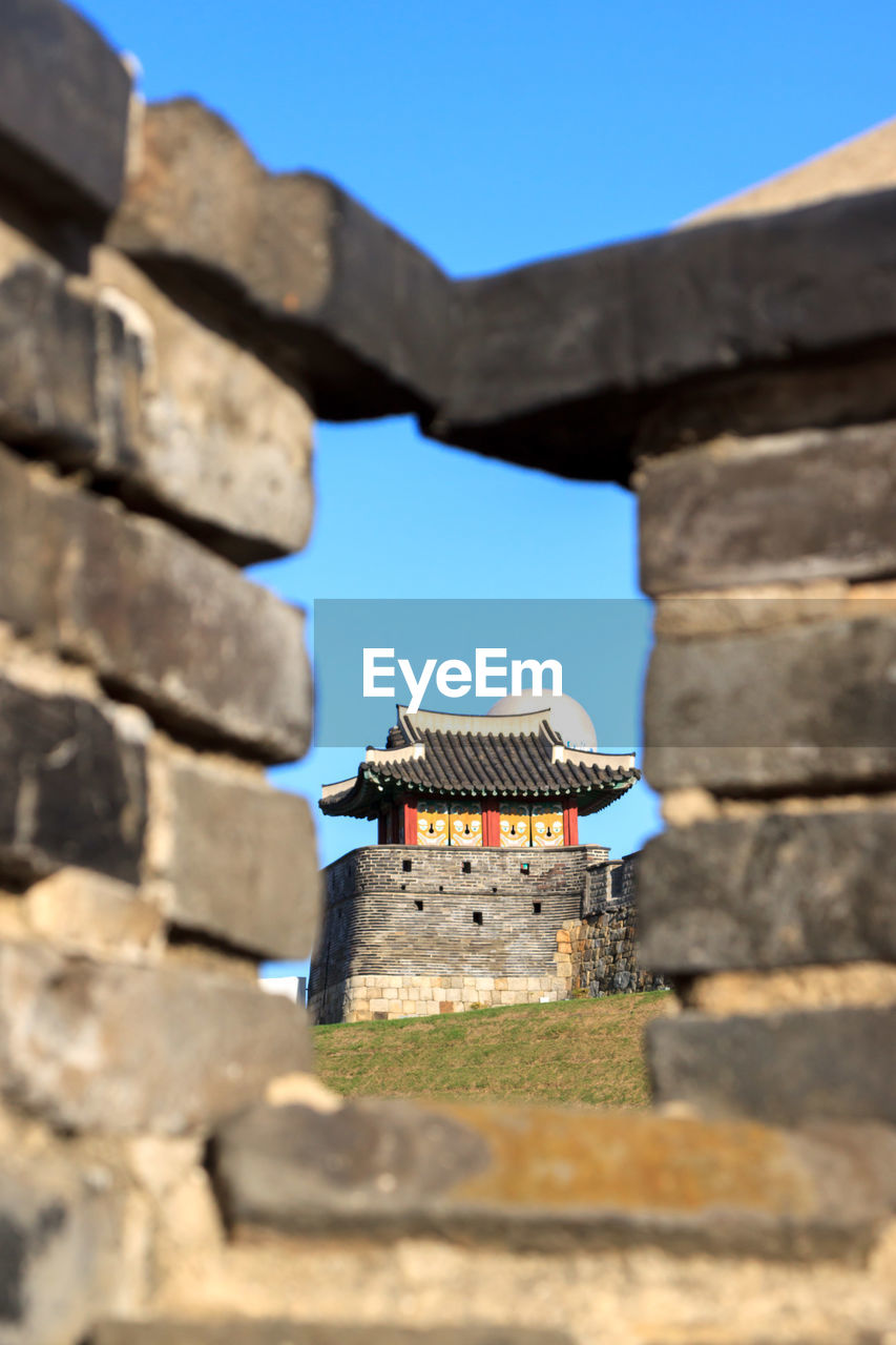 Low angle view of old korean guard tower building against blue sky framed by wall