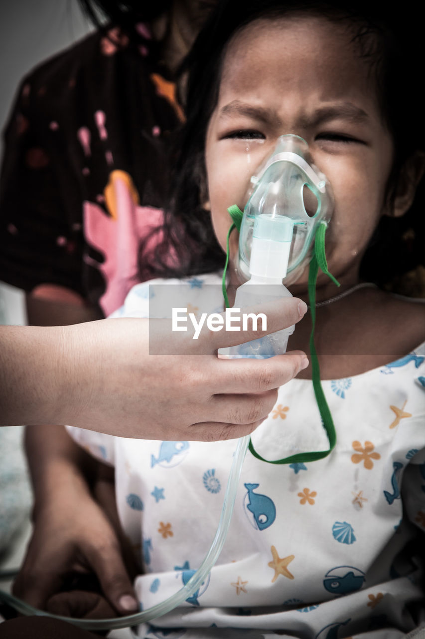 Cropped image of doctor putting mask on crying girl