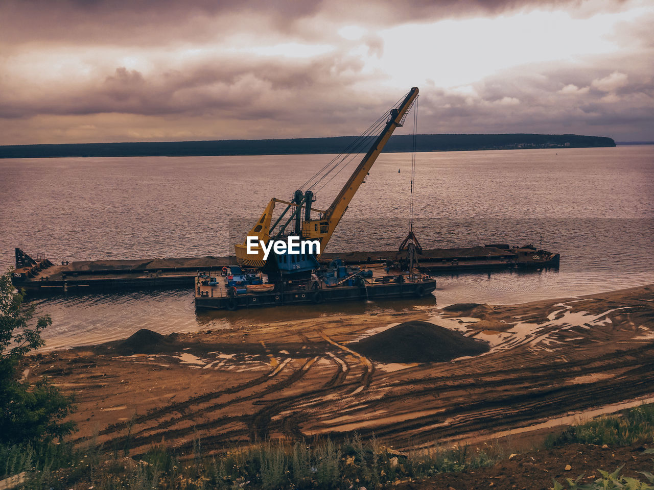 Construction site by sea against sky during sunset