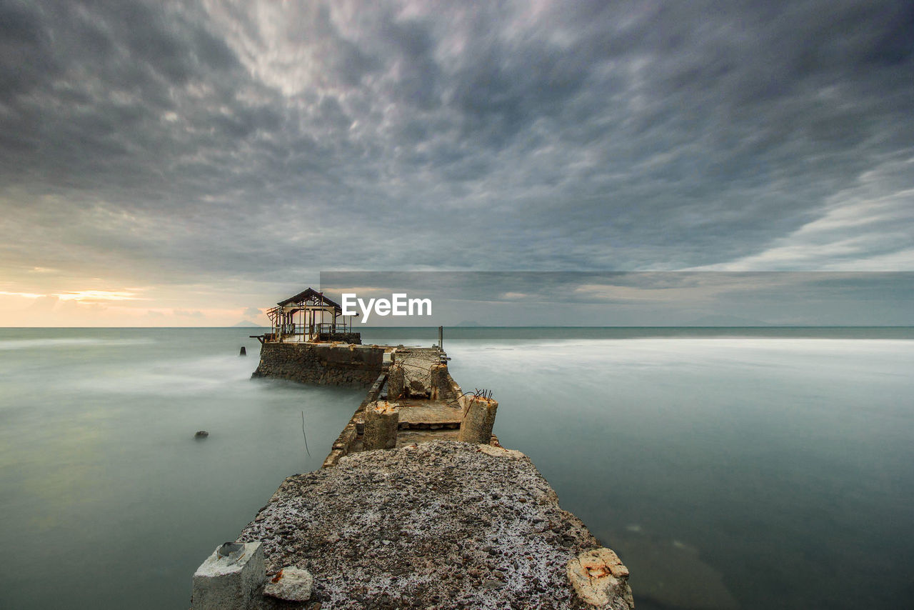 Damaged pier on sea against cloudy sky