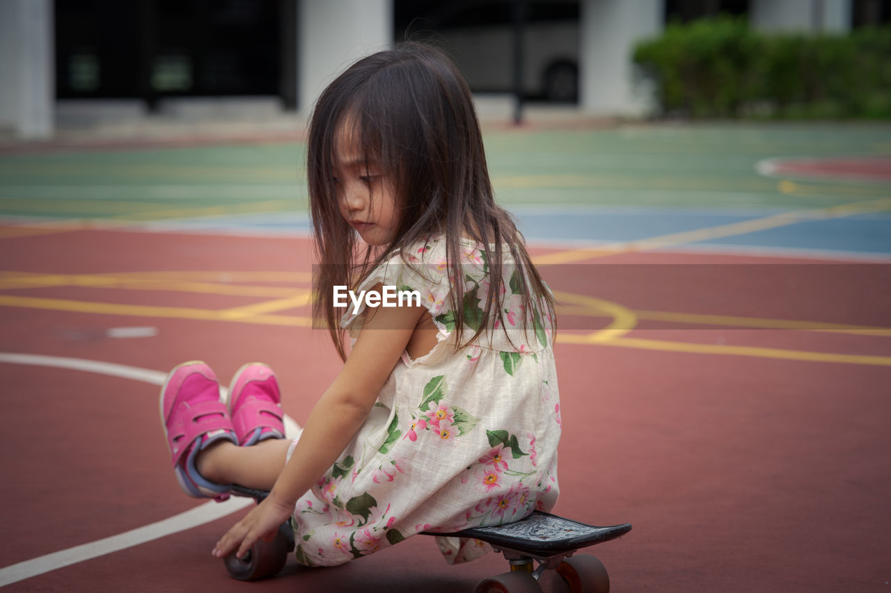 Rear view of cute girl playing with skateboard outdoors
