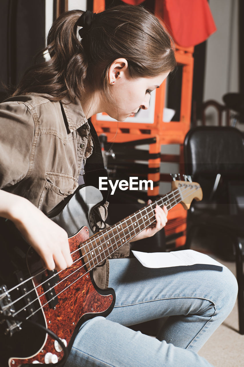 MIDSECTION OF WOMAN PLAYING GUITAR AT HOME