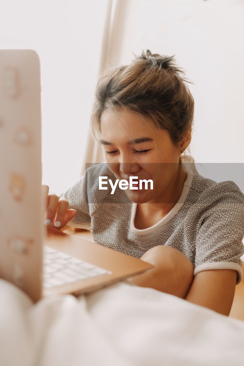 side view of young woman using laptop at home