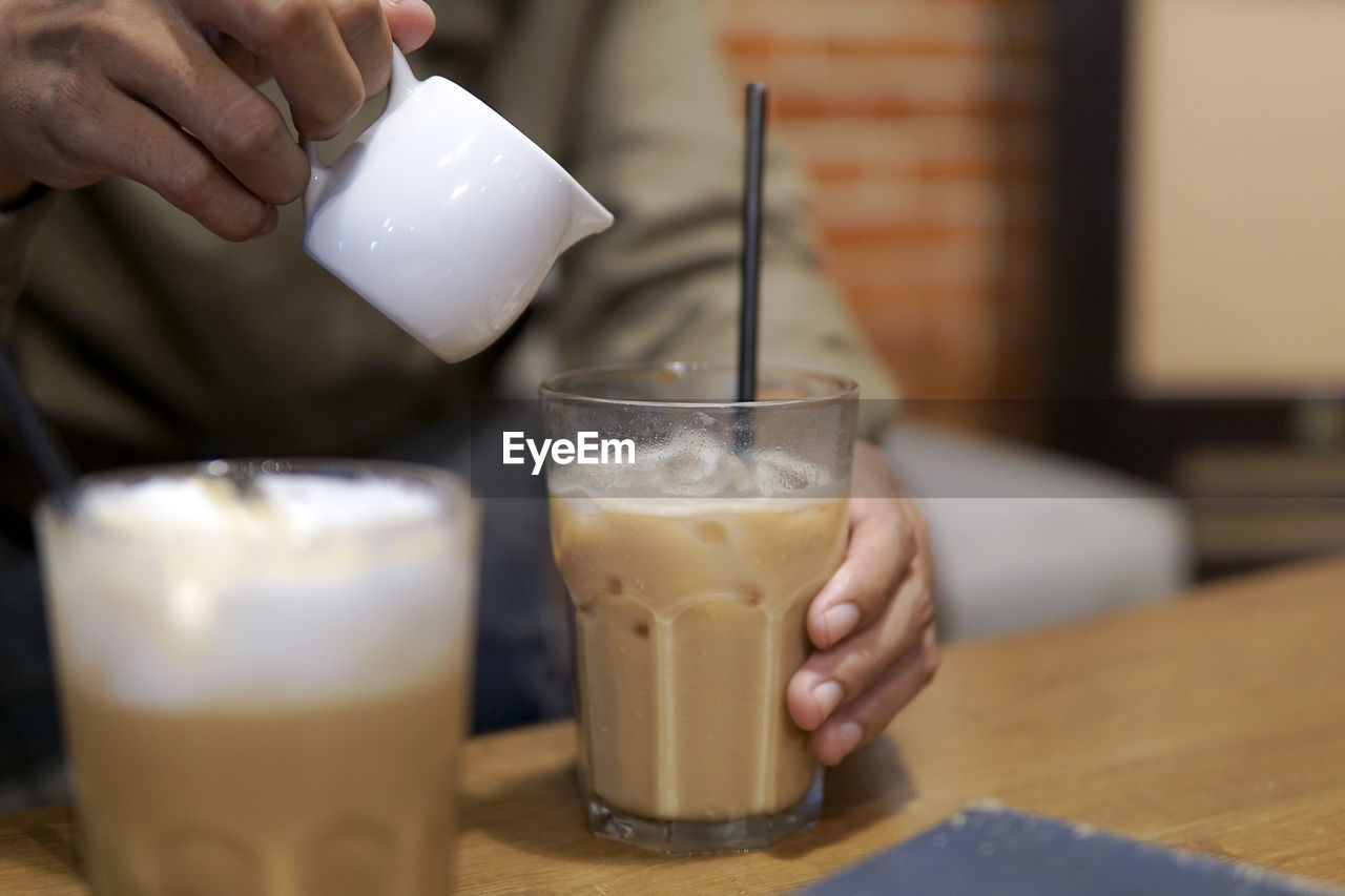 Cropped hands of man preparing iced coffee on table