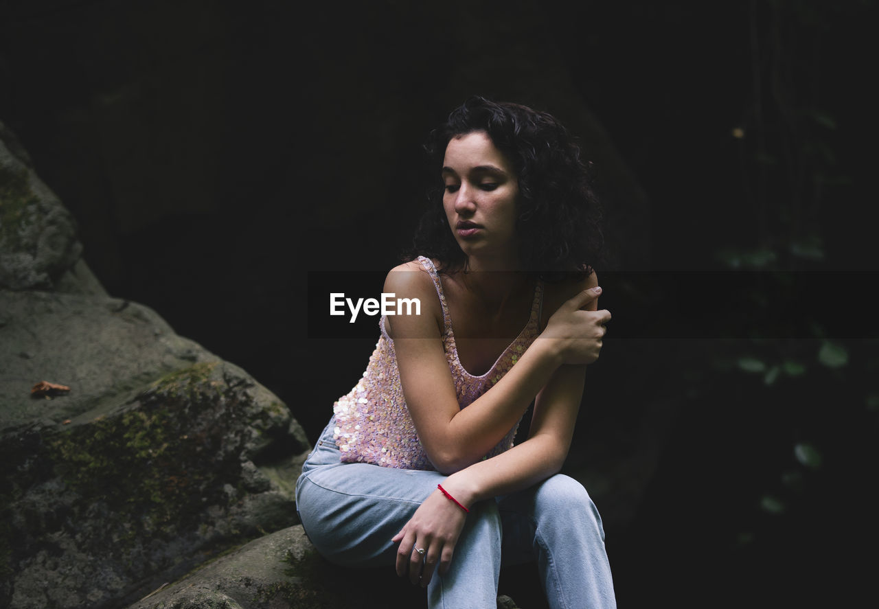 Young woman looking away while sitting on rock