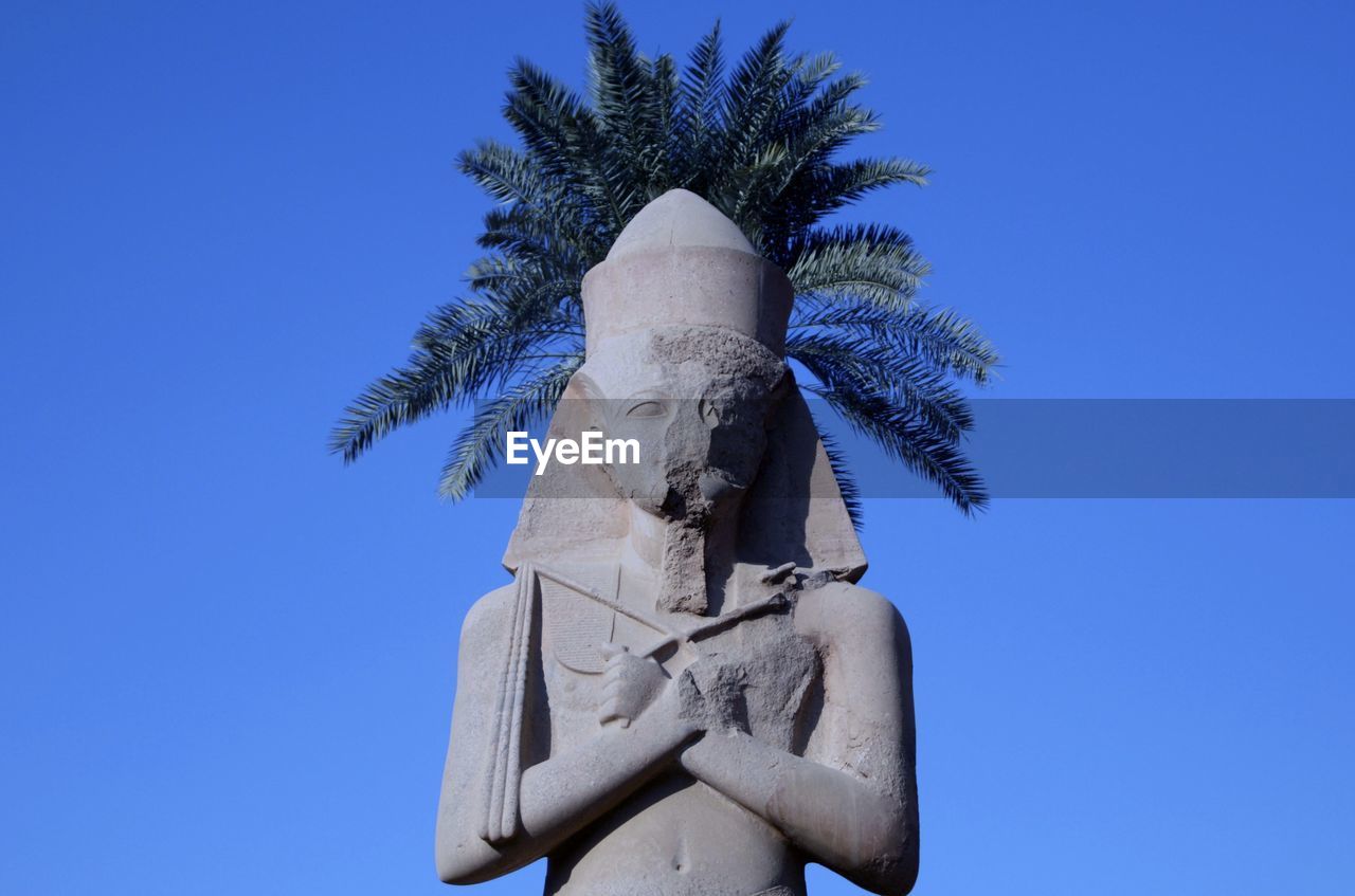 Low angle view of statue against blue sky with palm tree