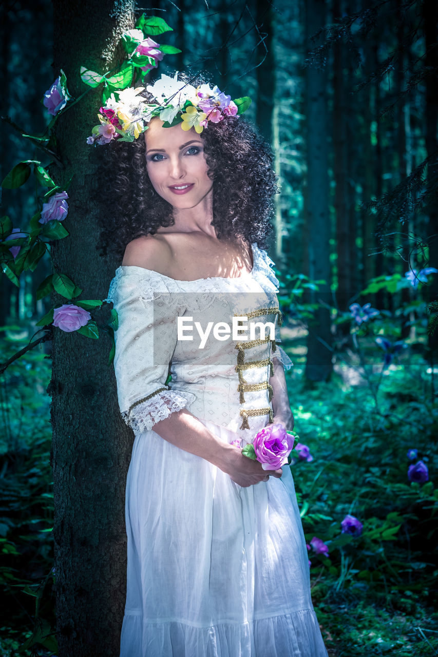 Portrait of mid adult woman wearing white dress while standing in forest