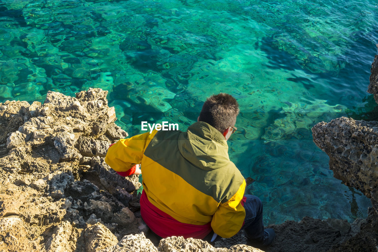 High angle view of man sitting on rock formation by sea