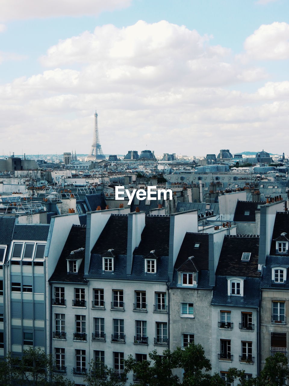 Distant view of eiffel tower in front of buildings against cloudy sky