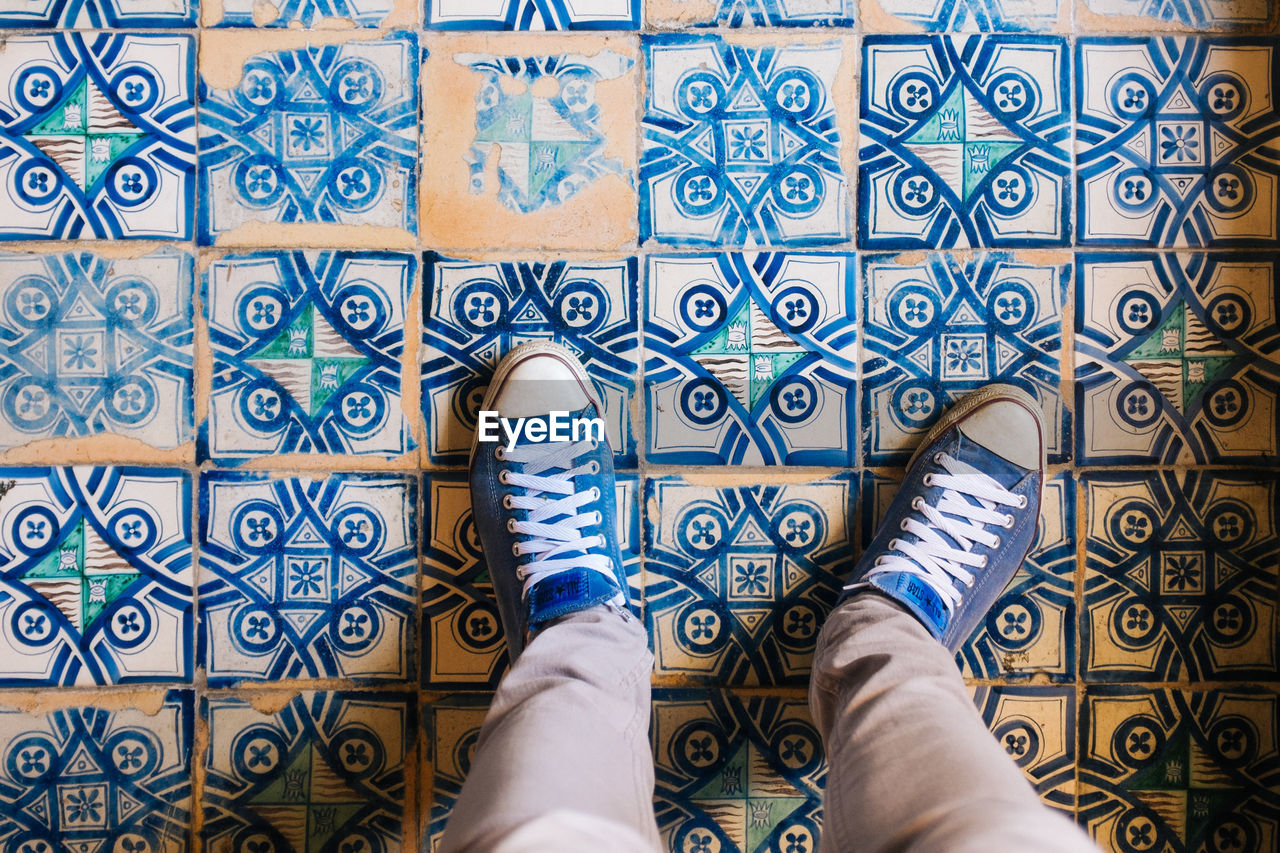 Low section of man in blue shoes standing on tiled floor