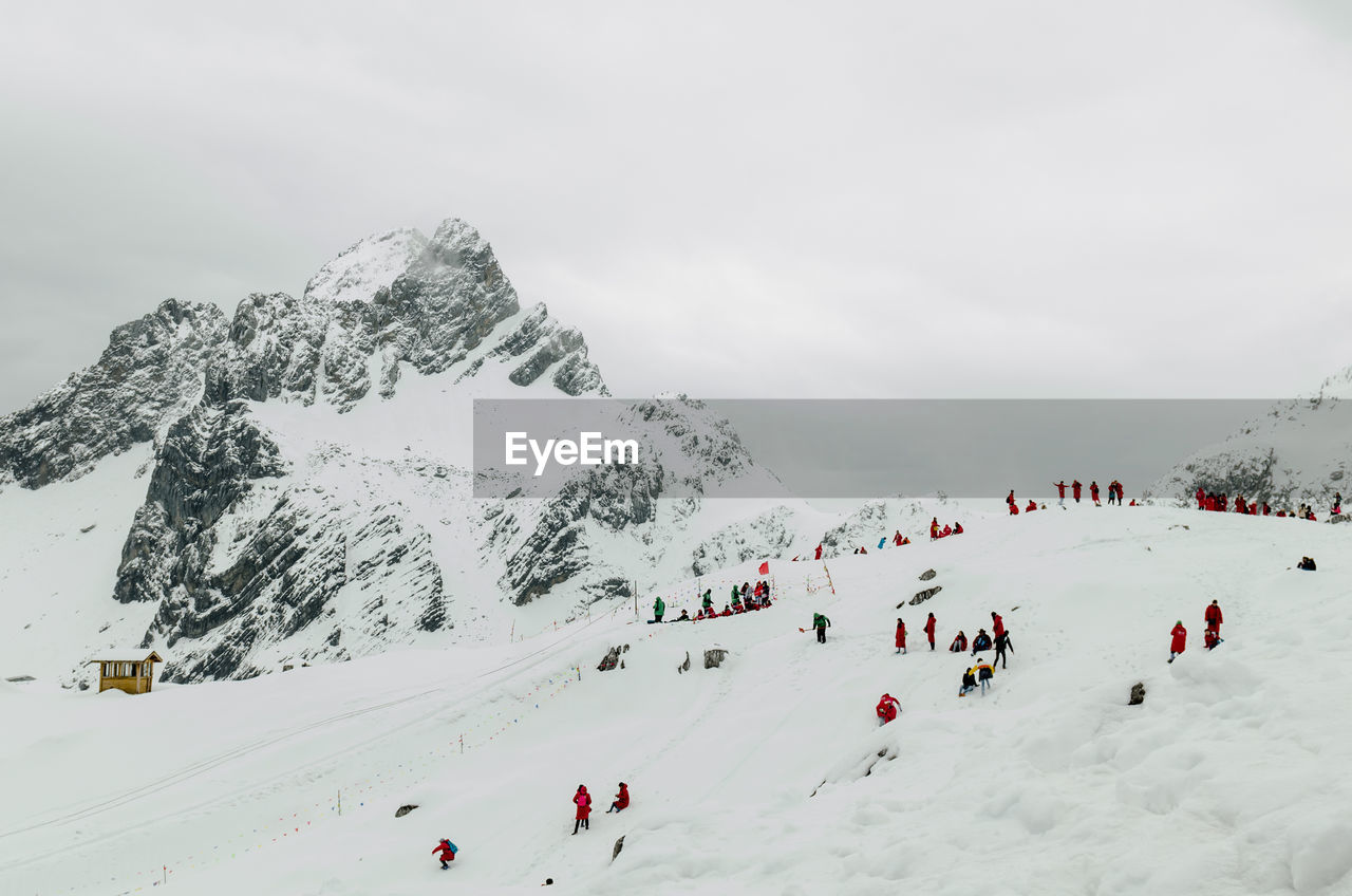Scenic view of people skiing against cloudy sky