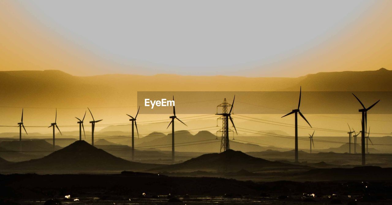 Windmills on landscape against sky during sunset