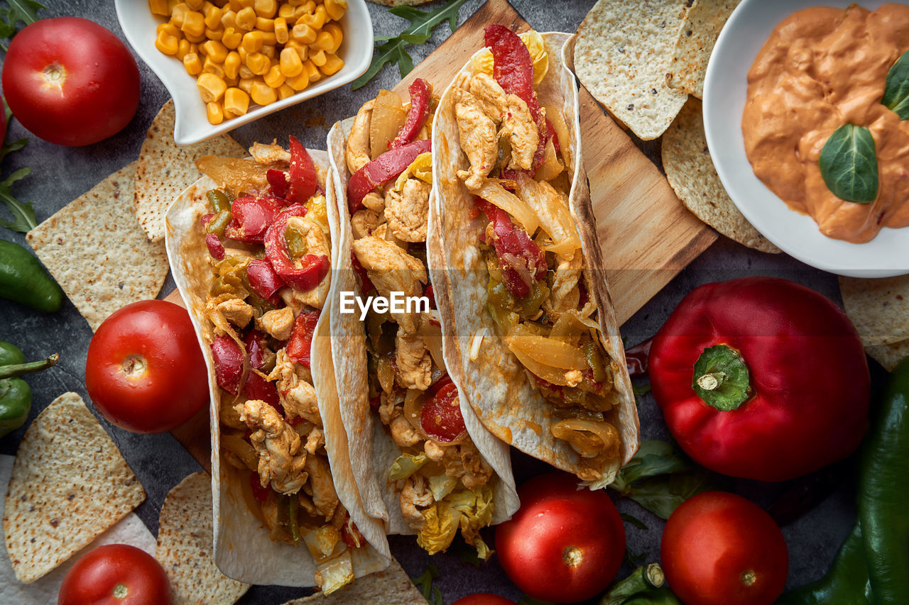 Still life of three fajitas or mexican tacos with meat, pepper, tomato, spicy pepper and nachos.