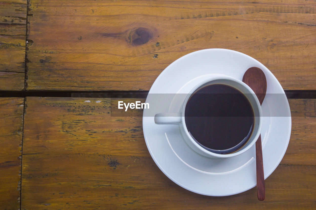 cup, food and drink, wood, mug, drink, table, coffee cup, coffee, crockery, refreshment, directly above, saucer, indoors, freshness, food, high angle view, hot drink, no people, still life, kitchen utensil, black coffee, copy space, eating utensil, tableware, spoon, wood grain