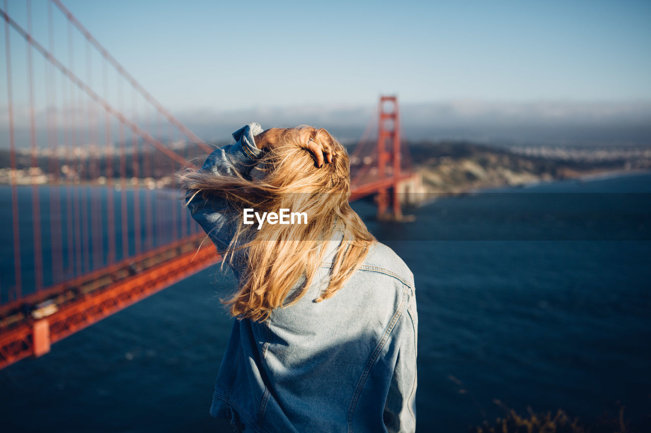 Rear view of woman standing by suspension bridge against sky