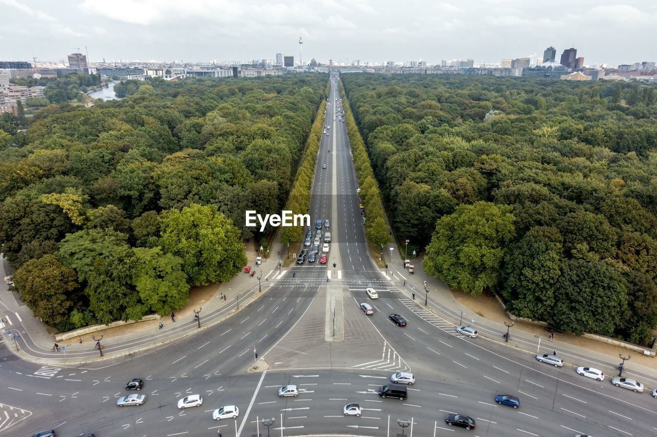 Vehicles on highway amidst trees in city against sky