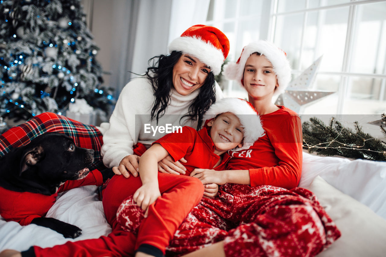 Smiling mother with kids and dog sitting on bed at home