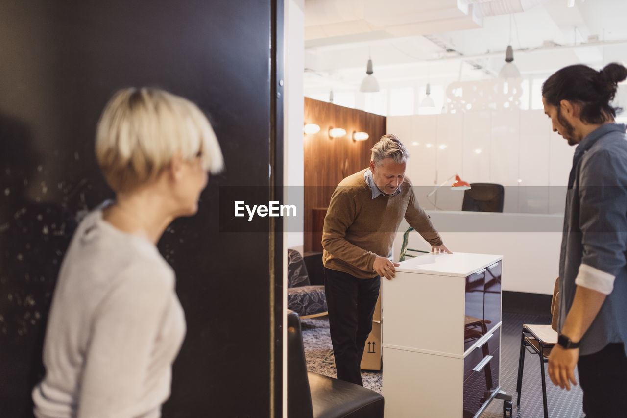 Business people looking at male colleague moving cabinet into new office