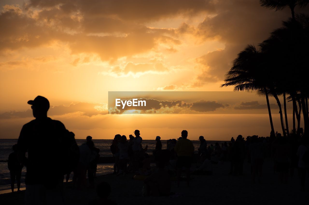 Silhouette of people on beach against cloudy sky