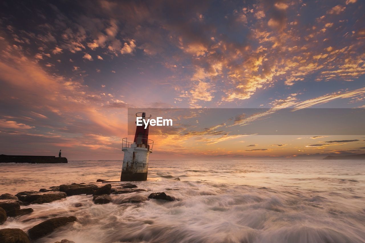 Lighthouse by sea against sky during sunset