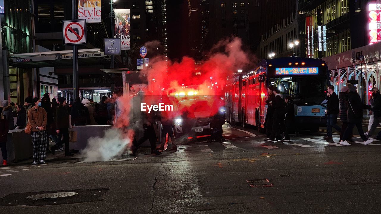 city, architecture, street, crowd, group of people, building exterior, night, riot, sign, transportation, built structure, communication, city life, city street, large group of people, road, smoke, car, illuminated, mode of transportation, outdoors, men