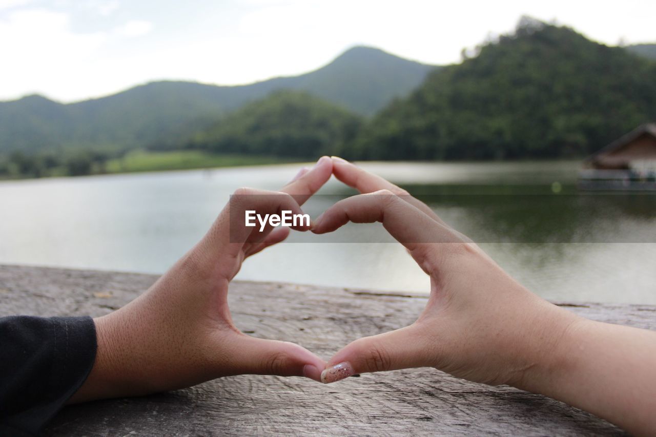 Cropped image of man and woman making heart shape by lake