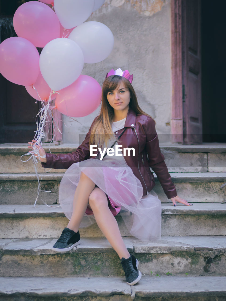 Portrait of young woman holding pink balloons while sitting on steps