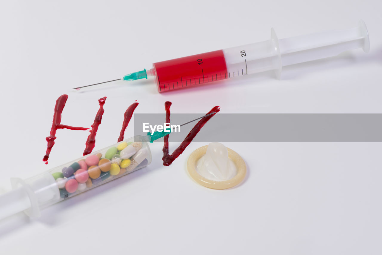 Close-up of syringe with condom on white background