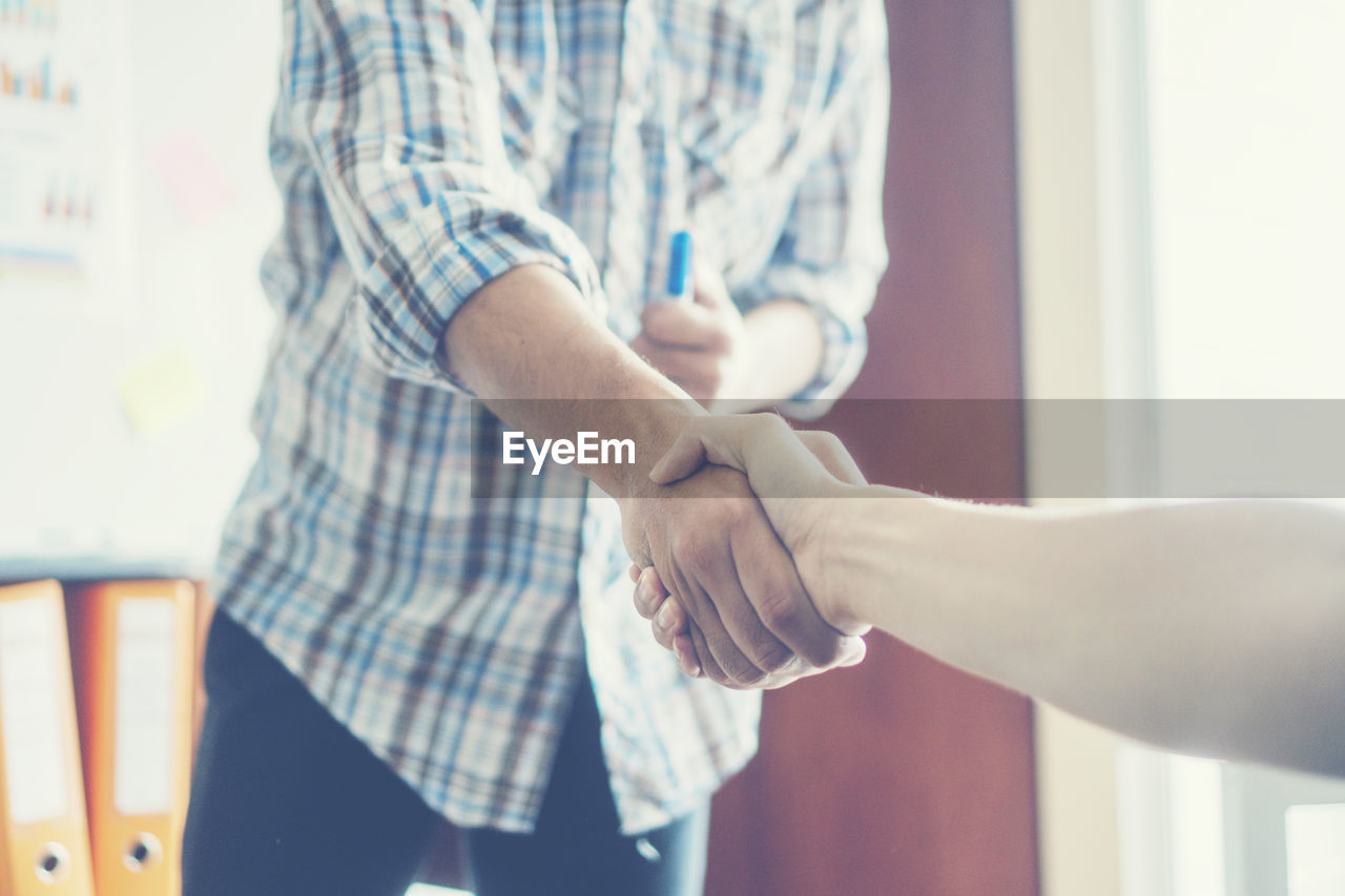 Cropped image of person shaking hands with male colleague in office