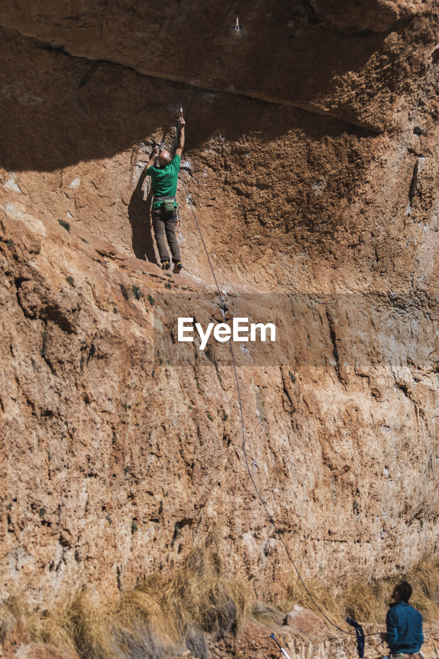 Climber attaching safety rope to a rock helped by a colleague