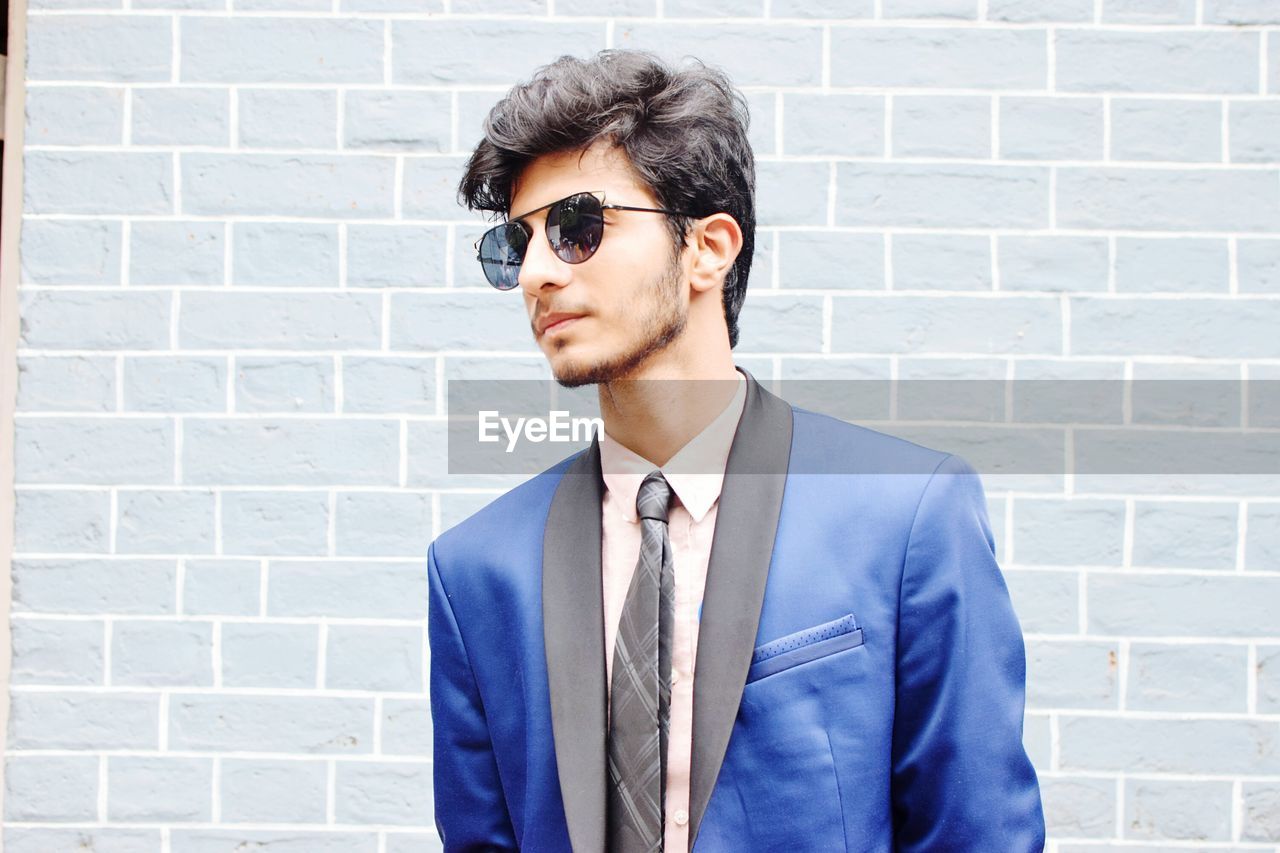 Young man wearing sunglasses standing against brick wall