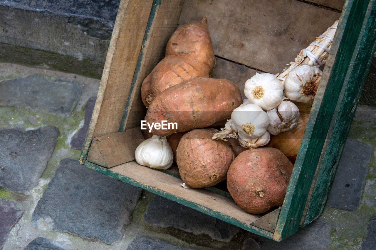 High angle view of sweet potatoes with garlics in wooden crate