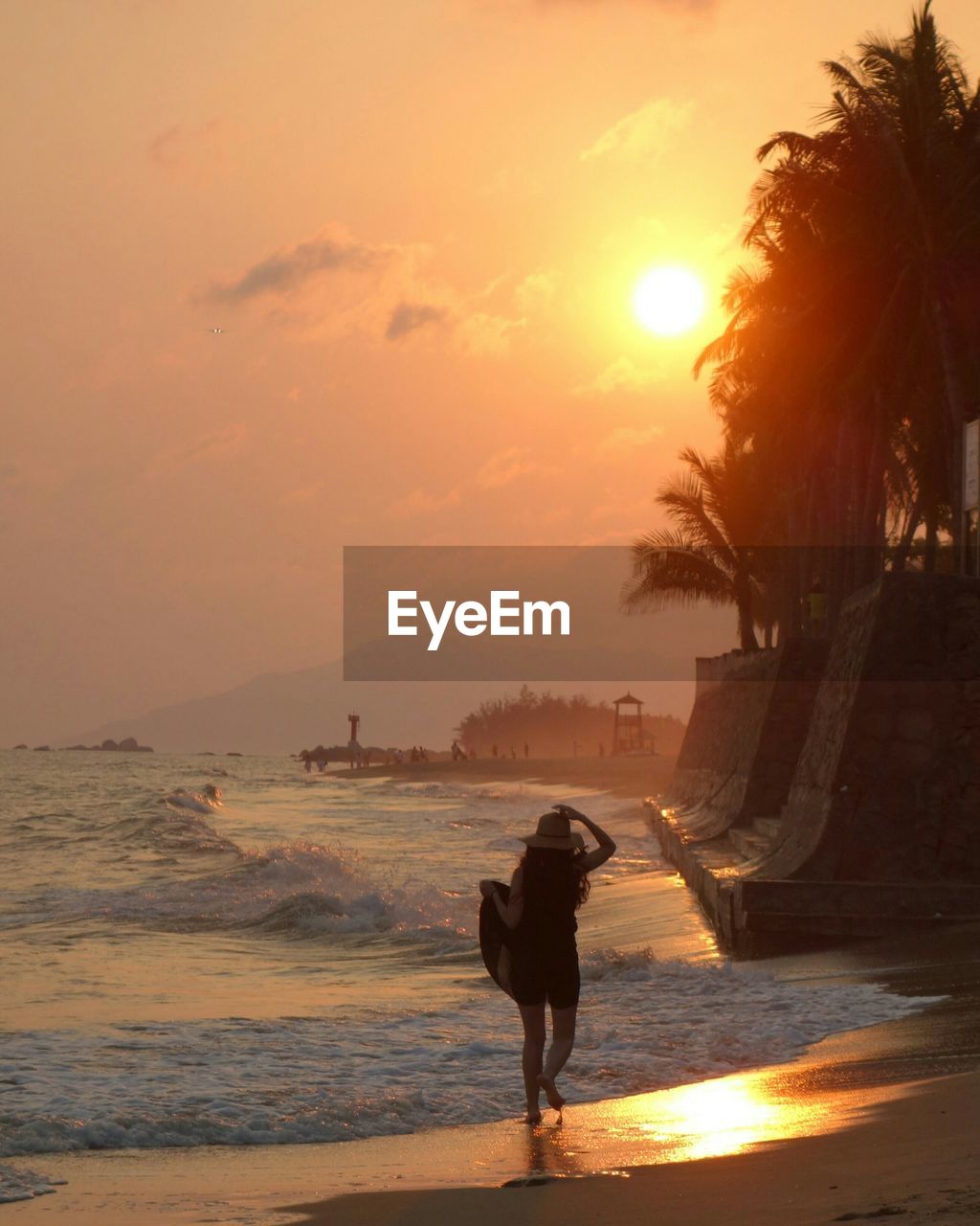 Rear view full length of woman walking at beach against sky during sunset