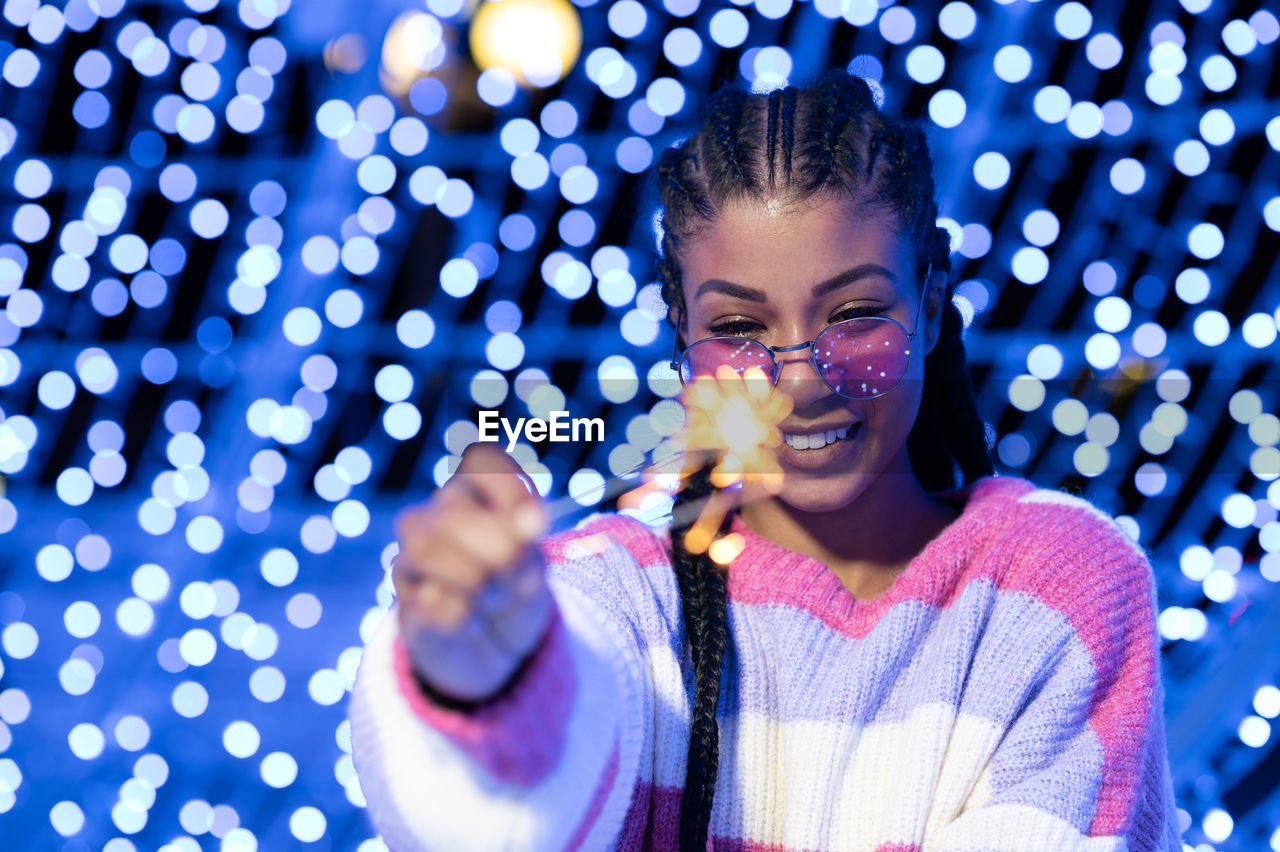 Cheerful black woman with braided hairstyle and pink glasses enjoying christmas lights