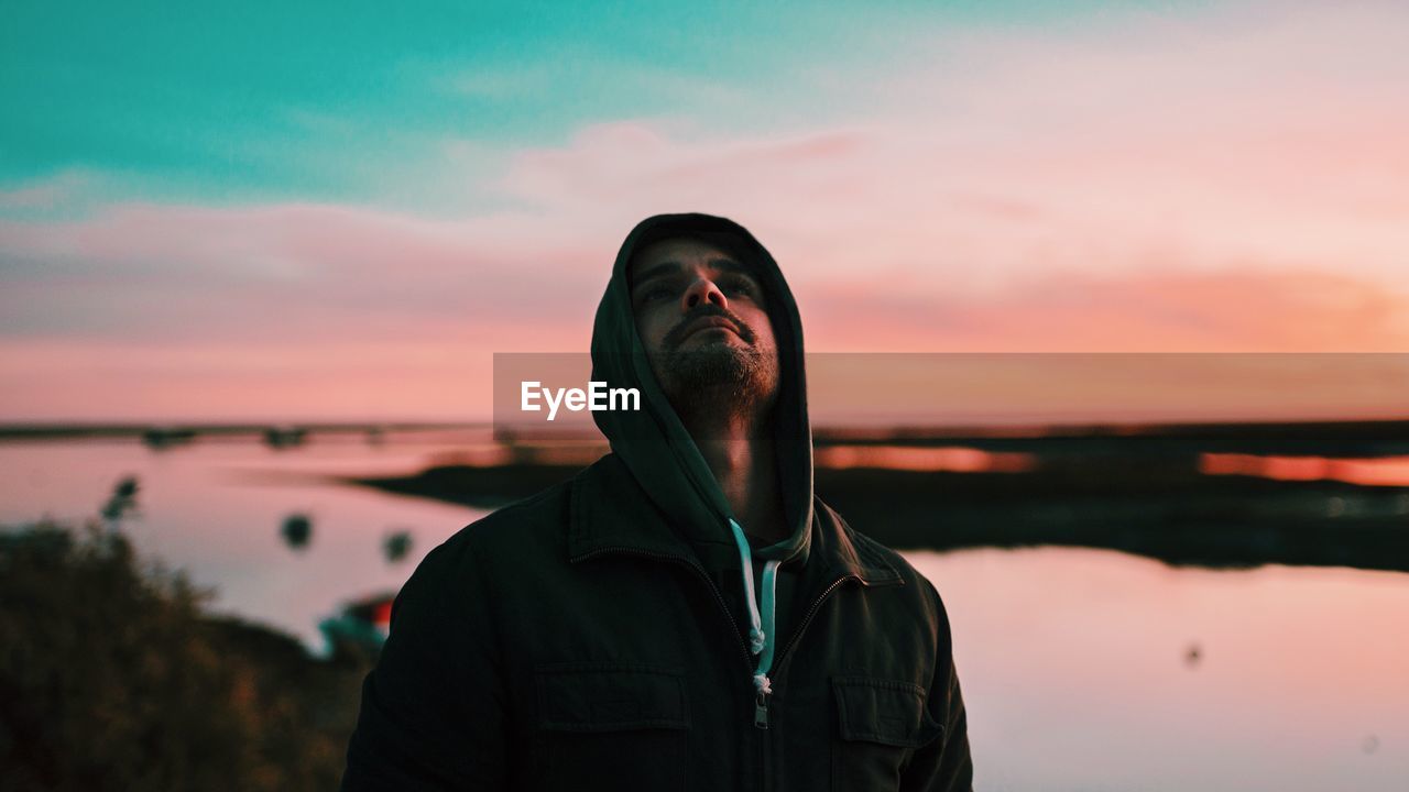 Man looking up while standing against lake during sunset