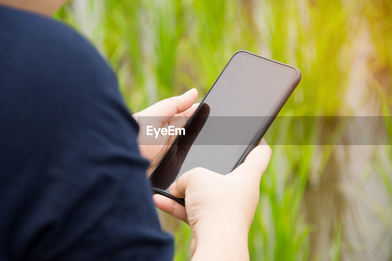 Cropped hands of man using mobile phone on field