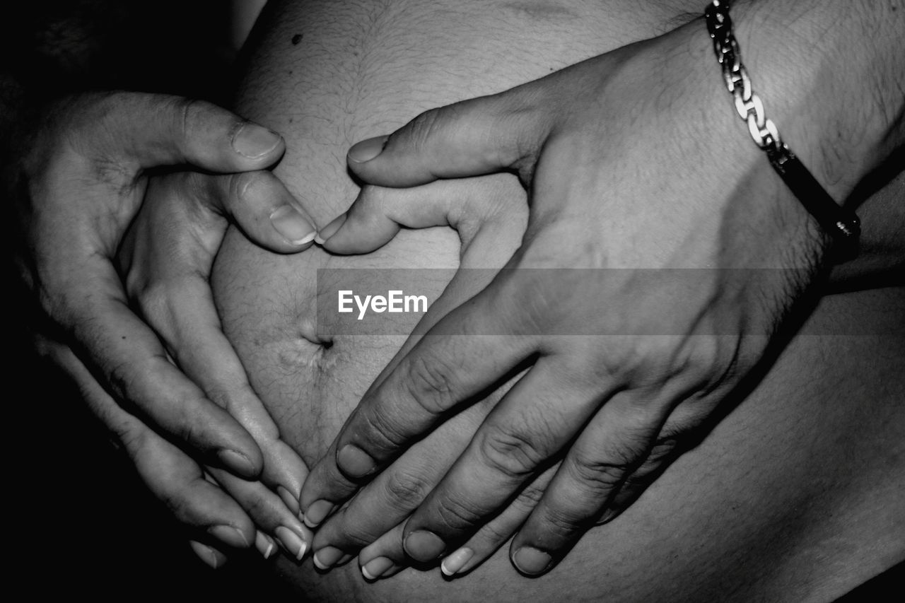 Midsection of couple making heart shape on stomach of pregnant woman