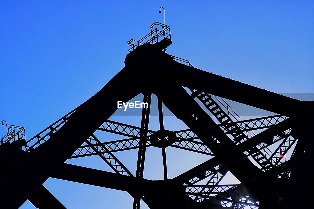 Low angle view of silhouette crane against clear blue sky