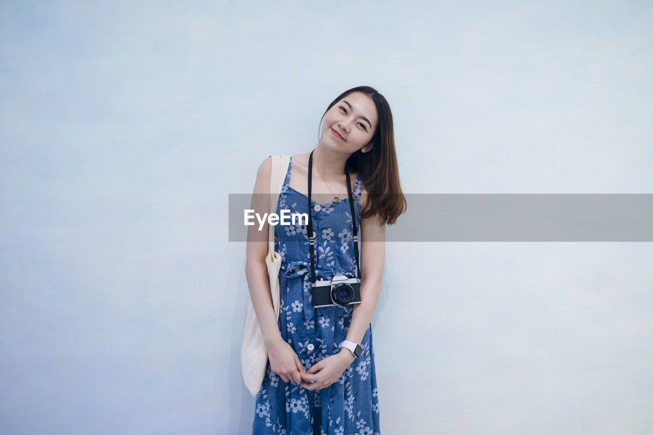 Portrait of smiling young woman standing against wall