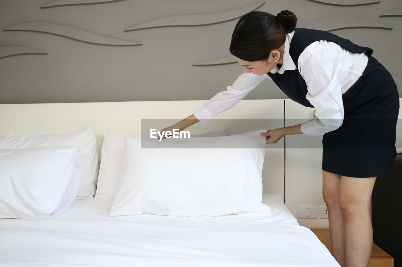 REAR VIEW OF WOMAN STANDING ON BED IN BEDROOM