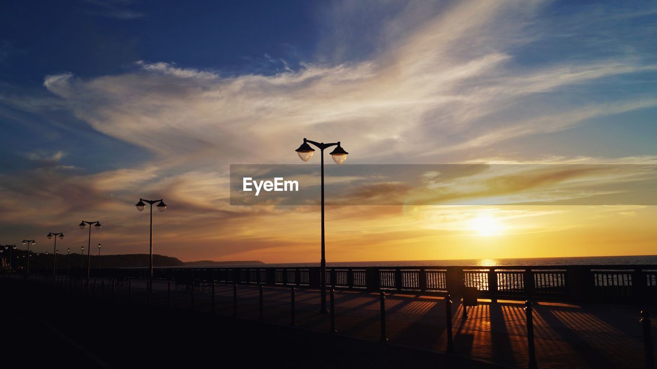 Silhouette street by sea against sky during sunset