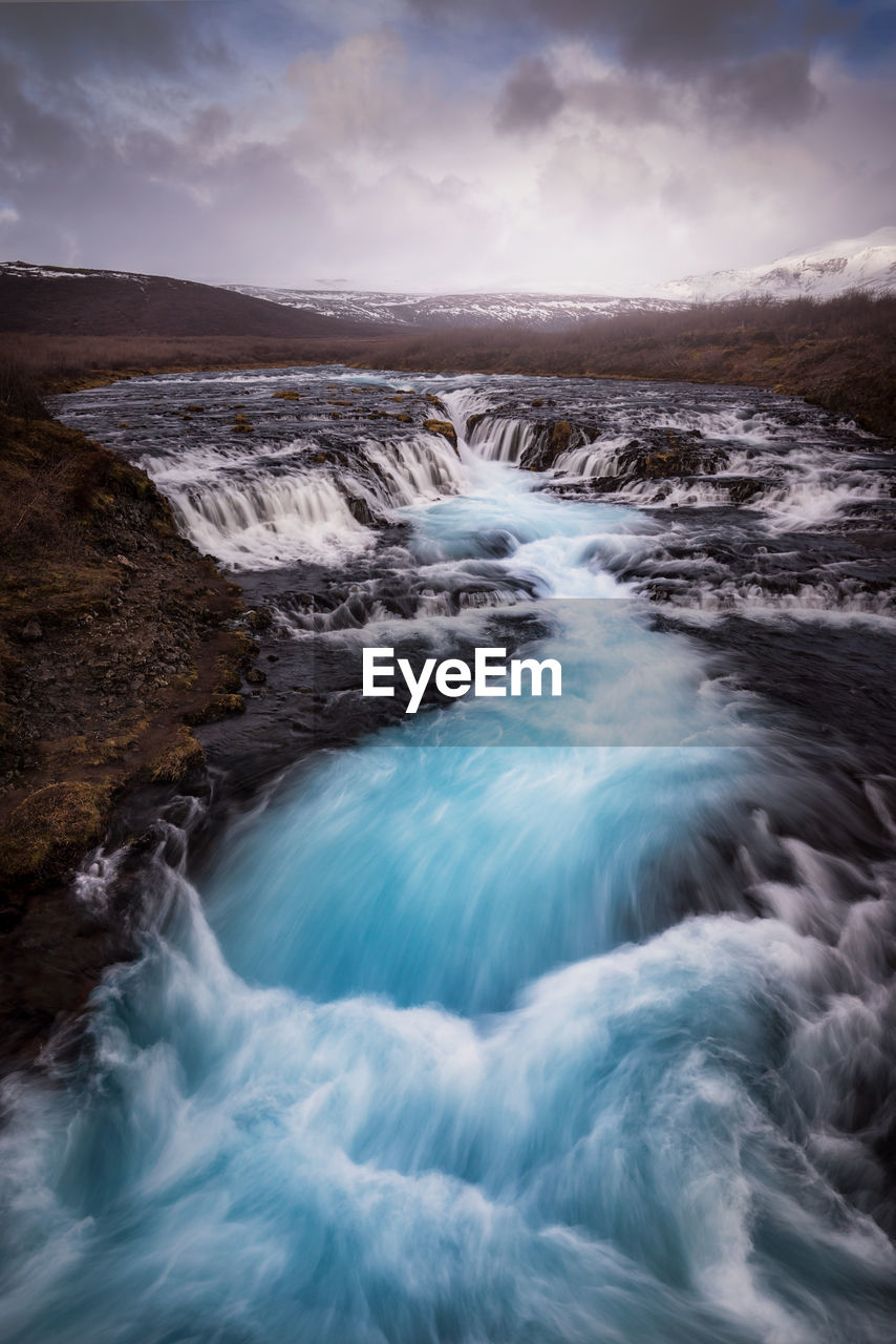 Scenic view of river flowing against cloudy sky