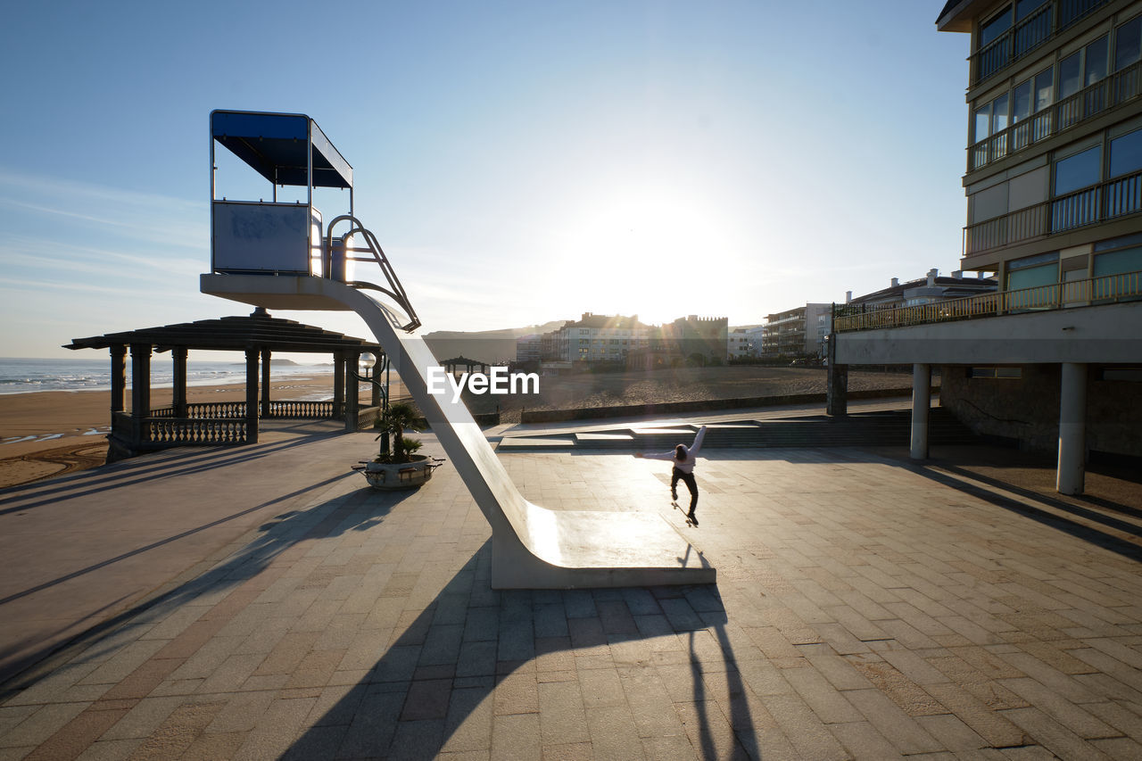 Side view of unrecognizable male skater riding down rescue tower located on seashore in summer