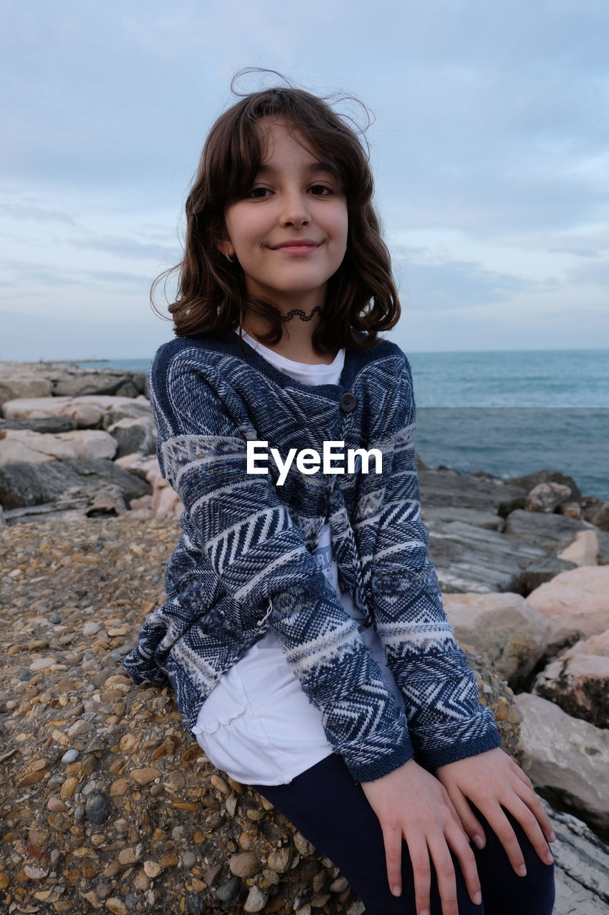 Portrait of smiling girl sitting on rock at beach 