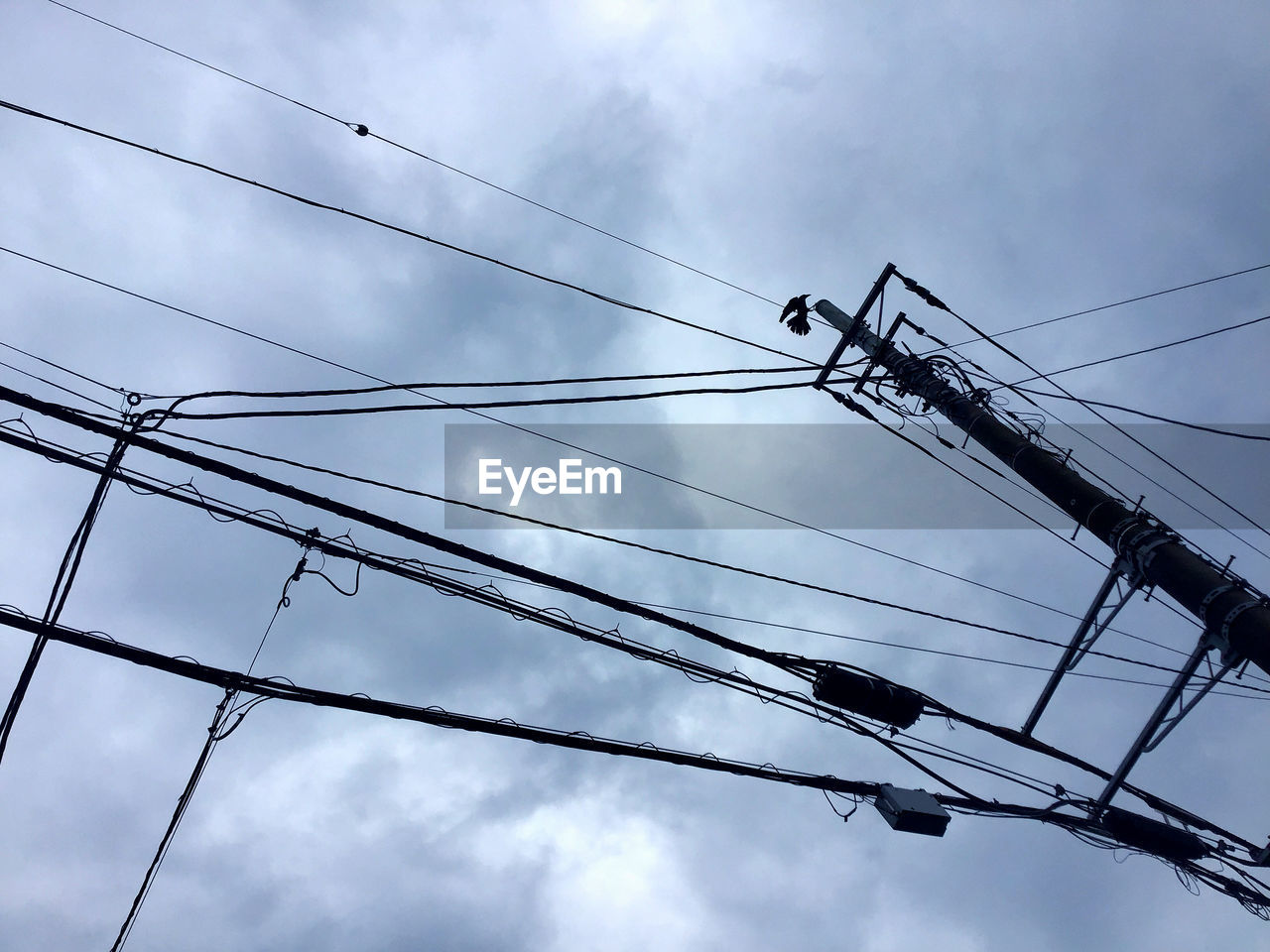 Low angle view of power lines against cloudy sky