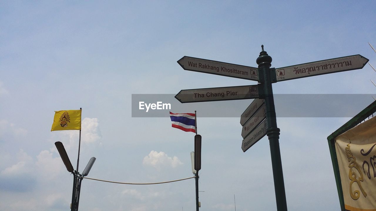 Low angle view of directional sign and thai flag against sky