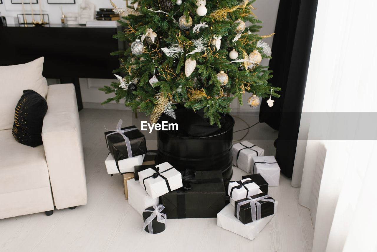Black and white gifts with bows lie under the christmas tree at home in the living room
