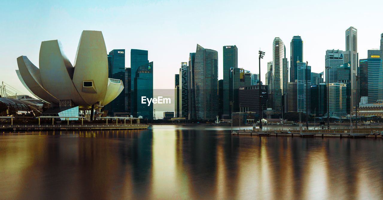 Modern buildings by river against sky in city