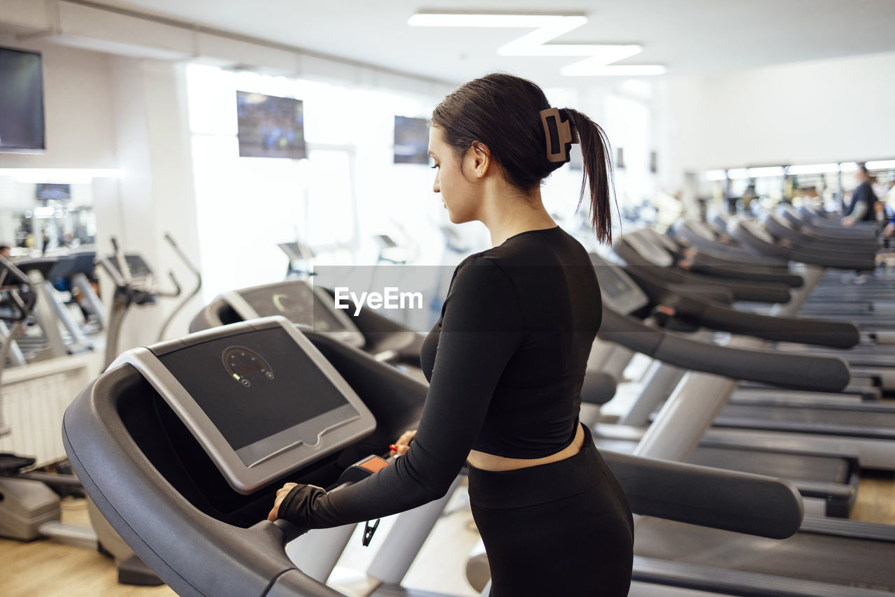 side view of young woman using mobile phone while standing in gym